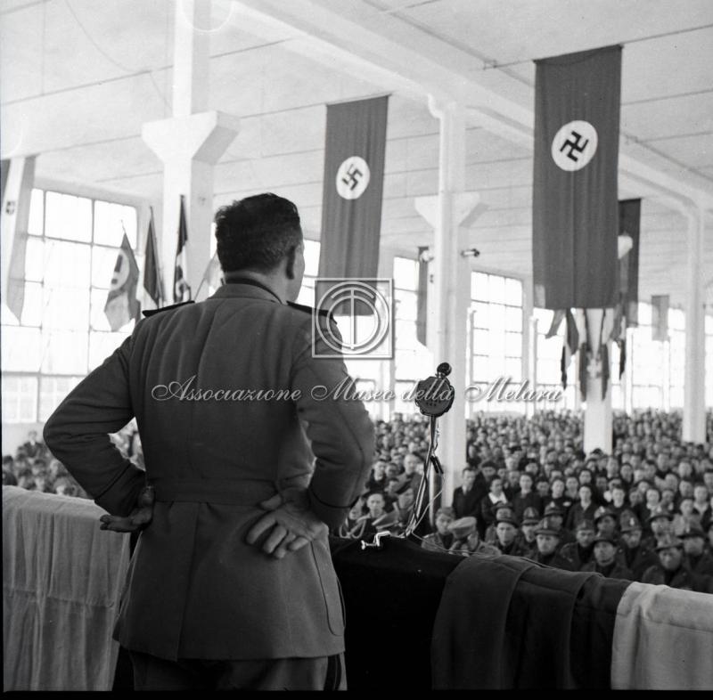 Gerarca di spalle mentre tiene il discorso al comizio fascista